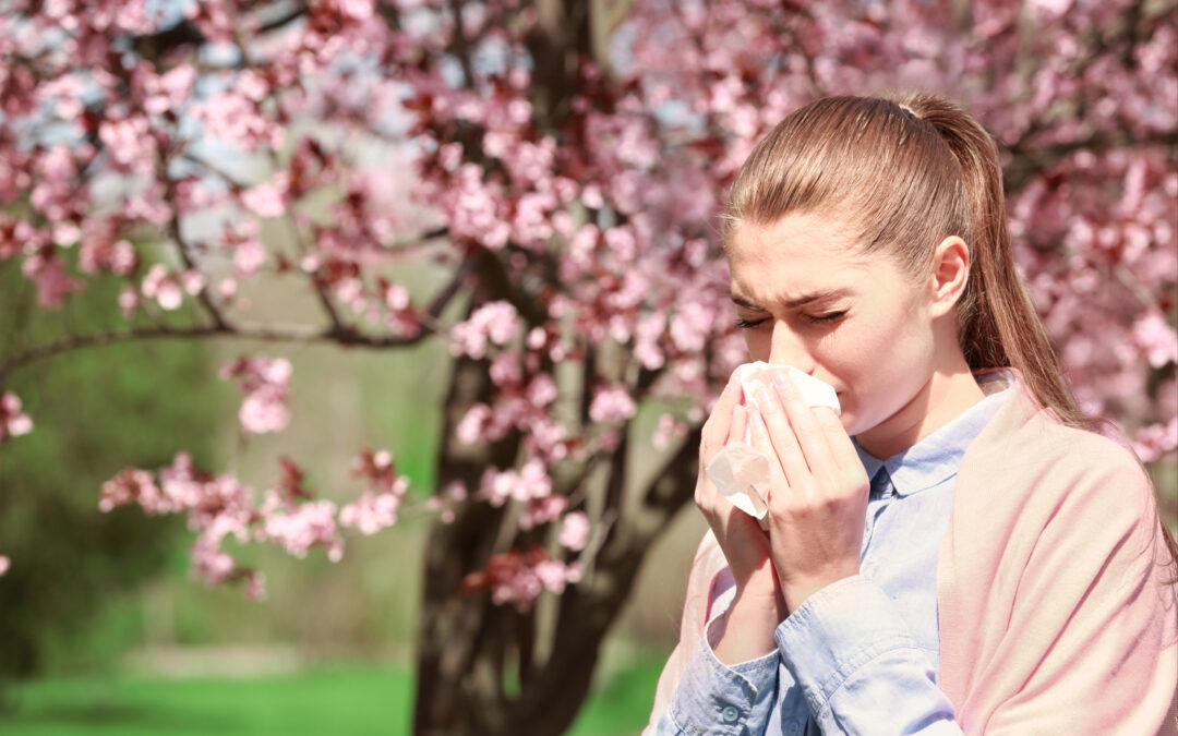 Woman in front of tree sneezing into tissue.